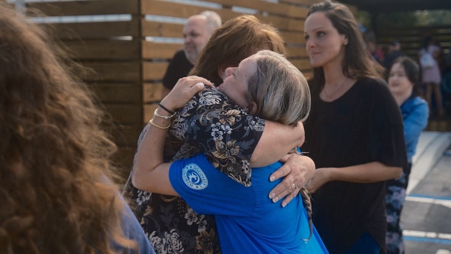 Two women embracing at Discovery Church on a Sunday morning, one wearing a Discovery Church shirt.